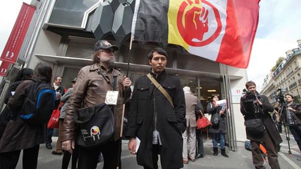 A French supporter of the Indian cause, who refused to give his name, left, holds a flag of the American Indian Movement and an American exchange student, member of the Arizona's Hopi tribe, Bo Lomahquahu, right, stand outside of the Druout's auction house to protest the auction of Native American Hopi tribe masks in Paris, Friday, April 12, 2013.