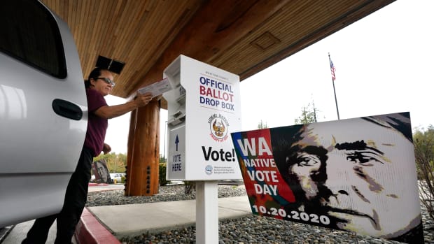 Lummi Nation tribal member Karen Scott drops her completed ballot into a ballot drop box Monday, Oct. 19, 2020, on the Lummi Reservation, near Bellingham, Wash. Washington Native Vote Day is Tuesday, Oct. 20, where tribes throughout the state connect, mainly remotely this year because of the coronavirus, with each other to encourage tribal members to register to vote and to cast their ballots. The historic photo used on the voting poster is referred to as "Lummi Woman," shot by Edward Curtis in 1899. It wasn't until 1962 that every state in the nation secured the right to vote for Native people. (AP Photo/Elaine Thompson)