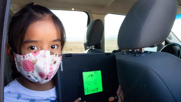 Second-grader Winona Begaye uploads homework in her family’s vehicle near Piñon. Navajo Nation schools have remained virtual this fall because it’s too dangerous to reopen their doors. To help families with no internet or poor access get online, the Piñon Unified School District outfitted school buses with Wi-Fi. (Photo by Megan Marples/Cronkite News)