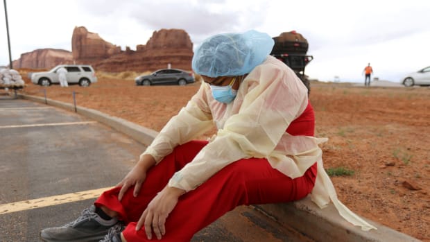 “My feet hurt,” says Denise Begaye, an X-ray technician with the Monument Valley Health Center, as she sits on a curb and takes a break from COVID-19 testing outside of the center in Oljato-Monument Valley, San Juan County on Thursday, April 16, 2020. The mobile testing team tested 581 people on Thursday. (Photo by Kristin Murphy, Deseret News via AP)