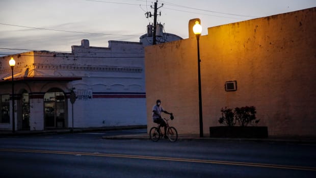 A man riding a bicycle down an empty street wears a protective mask amid the COVID-19 coronavirus outbreak on Friday, April 17, 2020, in Dawson, Ga. In the impoverished southwest corner of Georgia the virus quietly climbed to having some of the country's worst per capita death rates from COVID-19. The underlying health conditions that make COVID-19 so deadly are more prevalent for African American people and for rural people, and they are mostly both, so doubly disadvantaged when the virus tore through town. (AP Photo/Brynn Anderson)