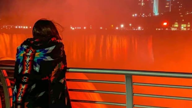 Kyrie Buffalo, 13, of the Seneca Nation (Turtle Clan), peers at the Canadian Horseshoe Falls while wrapped in a blanket on May 31, 2021. All three waterfalls, totaling about 800,000 gallons of water per second, were illuminated orange on Memorial Day in honor of the 215 children found in a mass grave at the site of the former Kamloops Indian Residential School in British Columbia. (Photo by Kateri Capton-Serpas via Ken Cosentino)