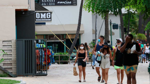 FILE - In this Aug. 24, 2021 file photo people walk past Waikiki restaurants and shops in Honolulu. The mayor of Honolulu says starting Sept. 13 the city will require patrons of restaurants, bars, museums, theaters and other establishments to show proof of vaccination or a recent negative test for COVID-19. (AP Photo/Caleb Jones, File)
