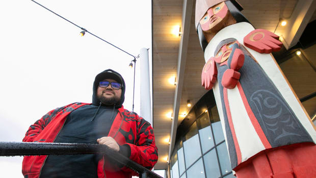 Ty Juvenil stands beside a welcome figure he created that was recently installed outside the Edmonds Waterfront Center on Friday, Nov. 25, 2022, in Edmonds, Washington. (Ryan Berry / The Herald)