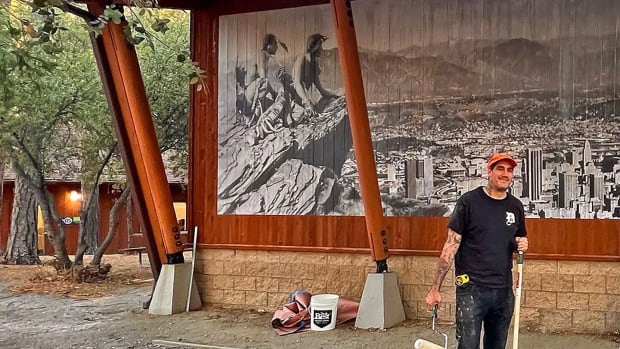 Artist Cheyenne Randall, Cheyenne River Sioux, installs a mural on an outdoor wall at the Idyllwild Art Center in California in time for an Indigenous Peoples Day celebration on Oct. 10, 2022. Randall is known for his “Shopped Tattoos,” where he layers tattoos that tell stories onto celebrities and historic figures while upending material and popular culture. His latest installation, “Cheyenne Randall: Paste, Present, Future,” at the Idyllwild Arts Foundation and the Native American Arts Center in California, will stay up until nature takes its toll on them. (Photo courtesy Idyllwild Arts Foundation)