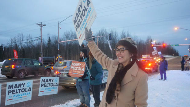 Rep. Mary Peltola waves campaign signs at passing motorists in East Anchorage on the morning of Election Day. The sealskin and otter-fur hat she is wearing was a gift from friends in Juneau. (Photo by Yereth Rosen/Alaska Beacon)