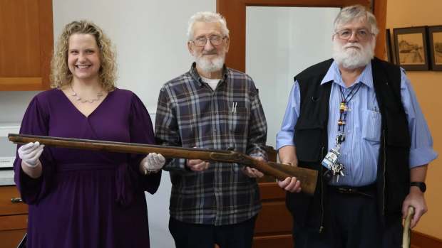 Newell Carson (center) along with his cousin Dr. Carson Gardner (right) present Beltrami County Historical Society Executive Director Emily Thabes (left) with a musket given to the family over a century ago by Shaynowishkung (He Who Rattles), also known as Chief Bemidji. (Mathew Holding Eagle ,MPR News )