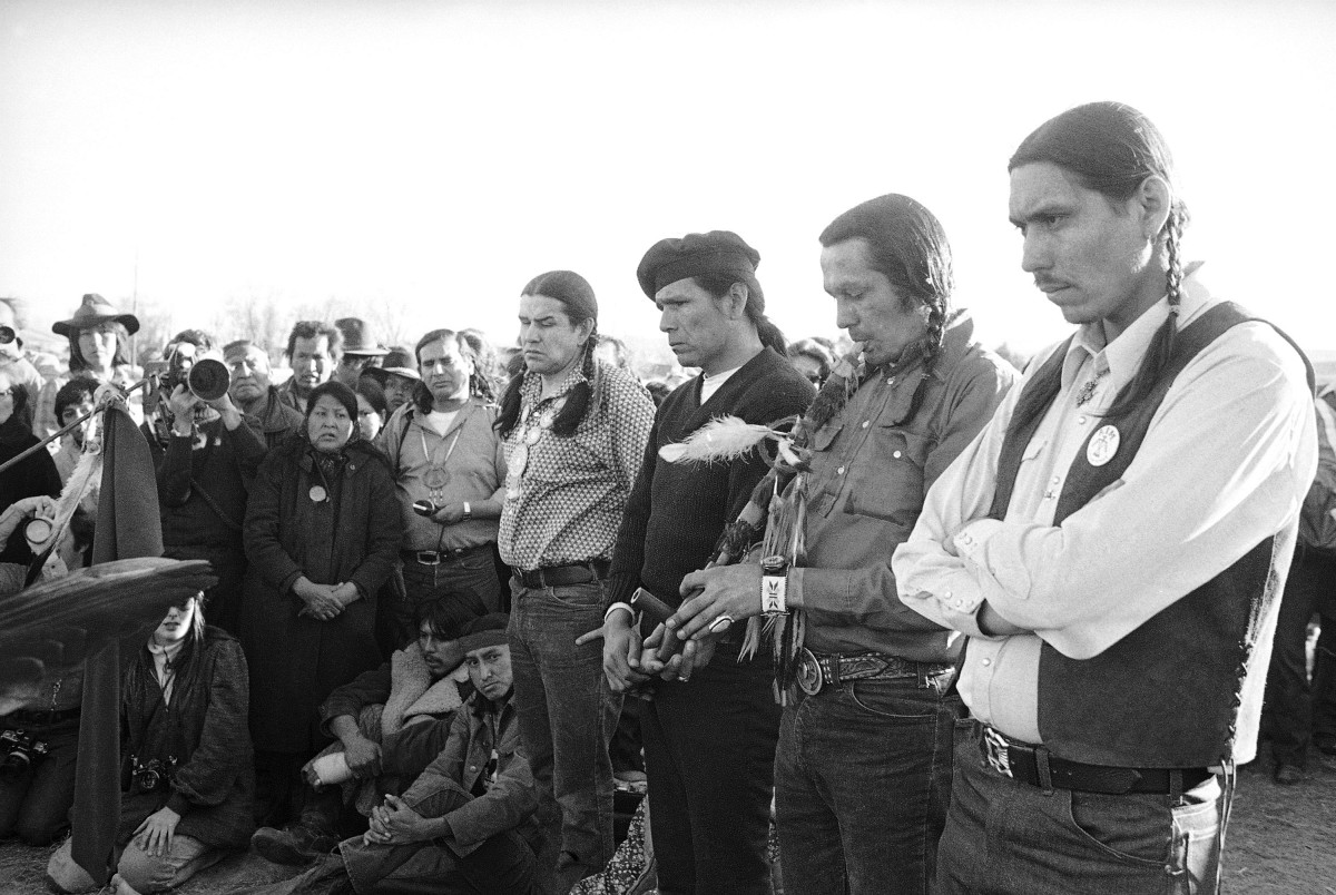 American Indian Movement leaders observe with a ceremonial peace pipe as the U.S. Department of Justice begins to remove government forces from around Wounded Knee, South Dakota,  with a ceremonial peace pipe smoking shown here on March 10, 1973. Shown are, starting with the fourth person from the right, AIM leaders Clyde Bellecourt, Dennis Banks, Russell Means and Carter Camp. (AP Photo/FILE)