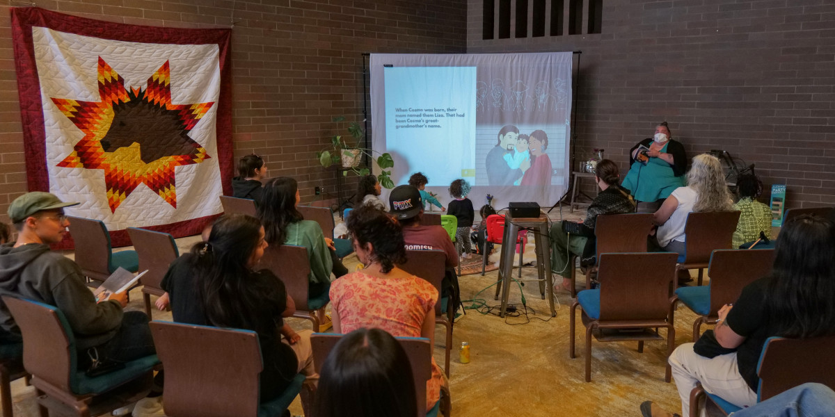 While performing the reading of "Cosmo, From the Stars," Shilo George, Southern Cheyenne and Arapaho descent, asks thoughtful questions to the audience about their experiences and feelings in relation to the book on Sept. 14, 2024 at Barbie's Village. (Photo by Jarrette Werk Underscore Native News / Report for America)