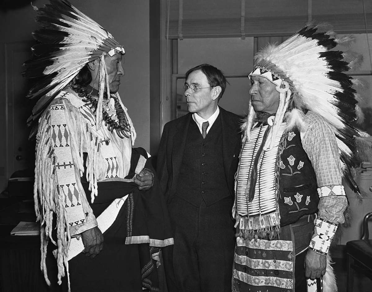 In full tribal regalia, Dewey Beard, left, and James Pipe-on-Head, survivors of the wounded knee creek massacre of 1890 in South Dakota, arrived in Washington on March 4, 1938, to testify in behalf of a bill to pay $1,000 to each of the survivors of the bloody fight in which 290 members of the Sioux Indian band were slain. They were greeted by John Collier, center, Commissioner of Indian Affairs. (AP Photo)