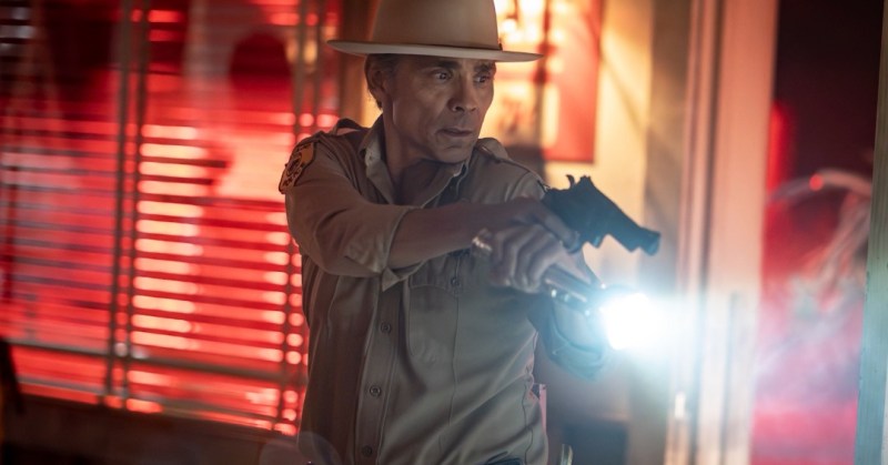 Zahn McClarnon holding gun and flashlight inside dark building in Dark Winds Season 4