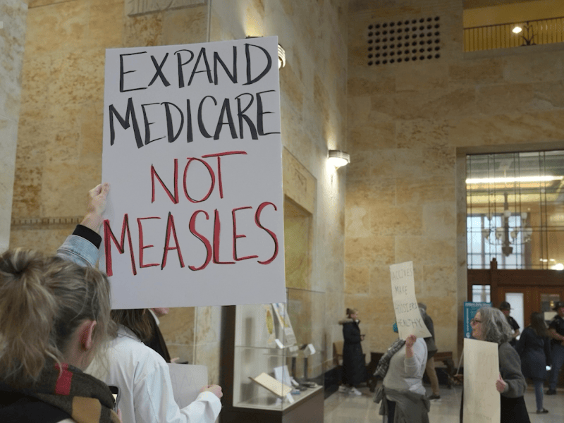 woman holds sign that reads expand medicare not measles