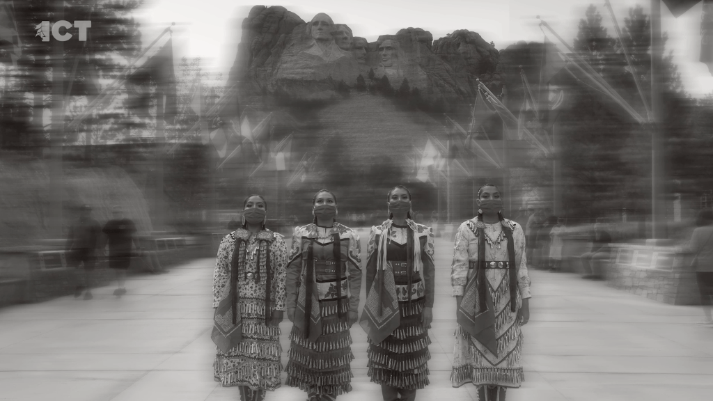 women in jingle dresses stand in front of mount rushmore national memorial